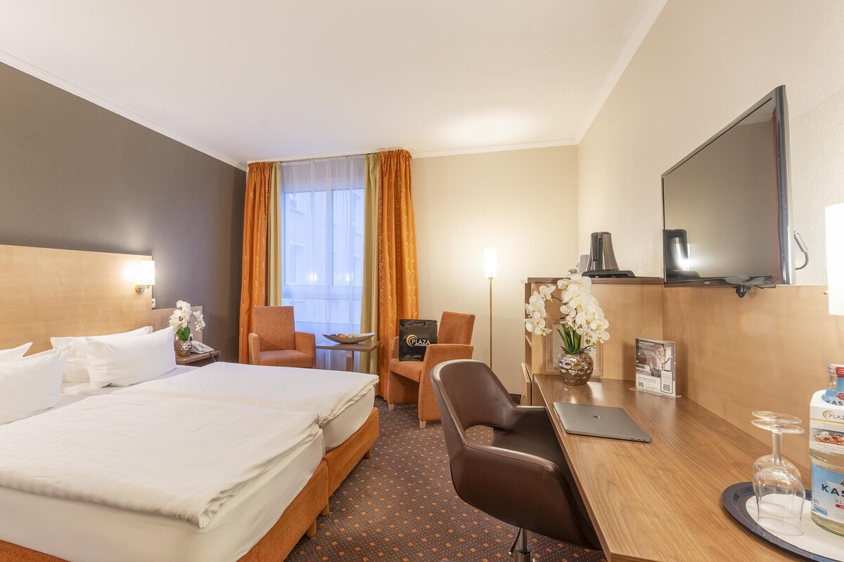 A hotel room with a large bed, a desk with a chair, a television, and a minibar.