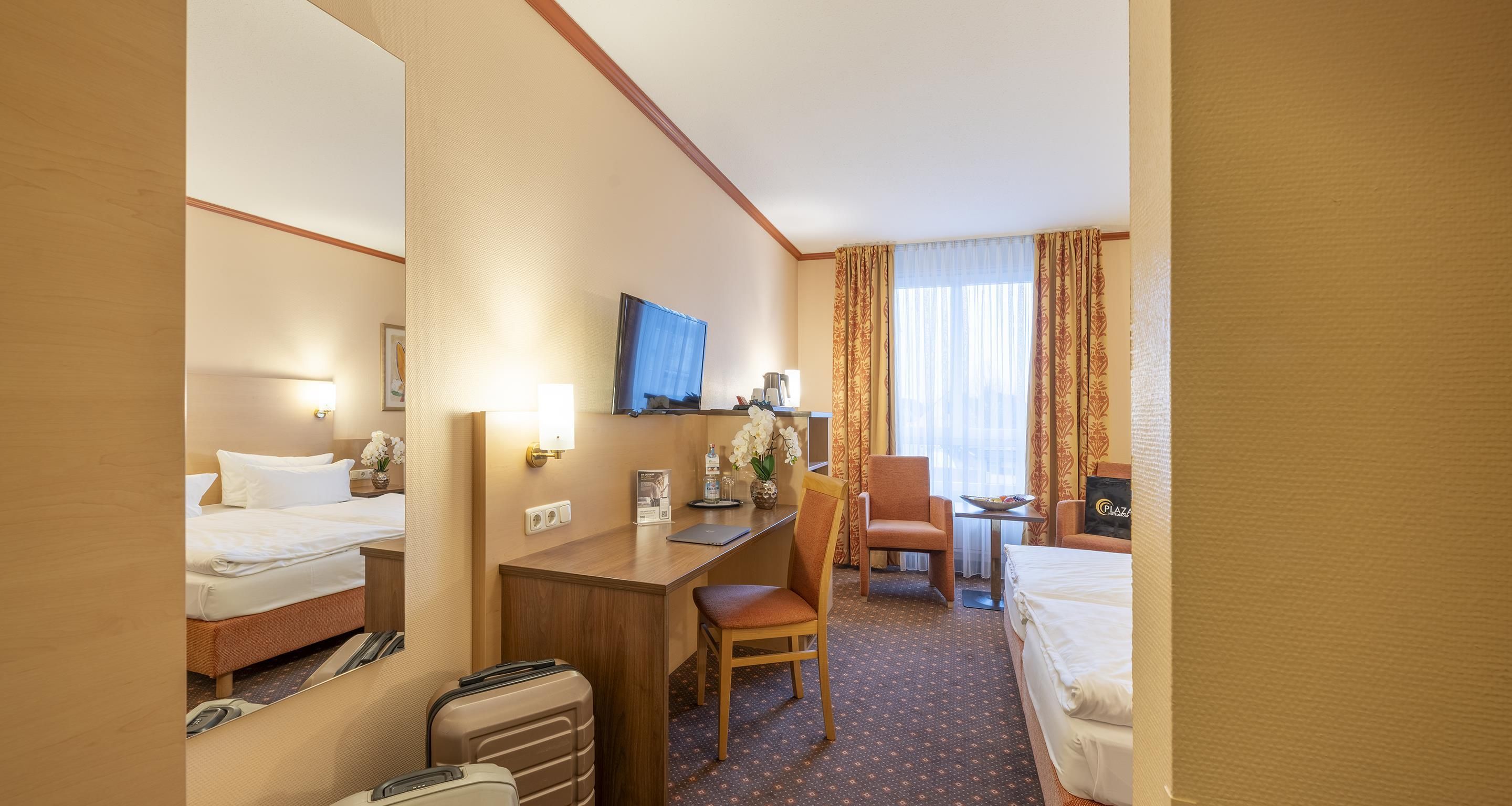 A hotel room with two beds, a desk, a chair, a TV, and a window with curtains.