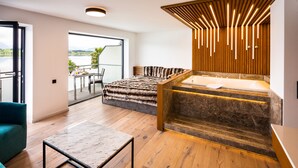 A modern room with a large bed, a sitting area, a wooden floor, and a view of the outdoors. - Hotel Am Hopfensee (Fuessen)