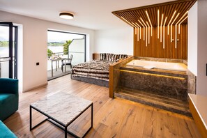 A modern room with a large bed, a sitting area, a wooden floor, and a view of the outdoors. - Hotel Am Hopfensee (Fuessen)