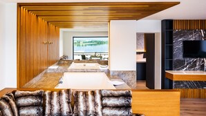 A modern bathroom with a large bathtub, wooden paneling, a marble countertop, and a TV mounted on the wall. - Hotel Am Hopfensee (Fuessen)