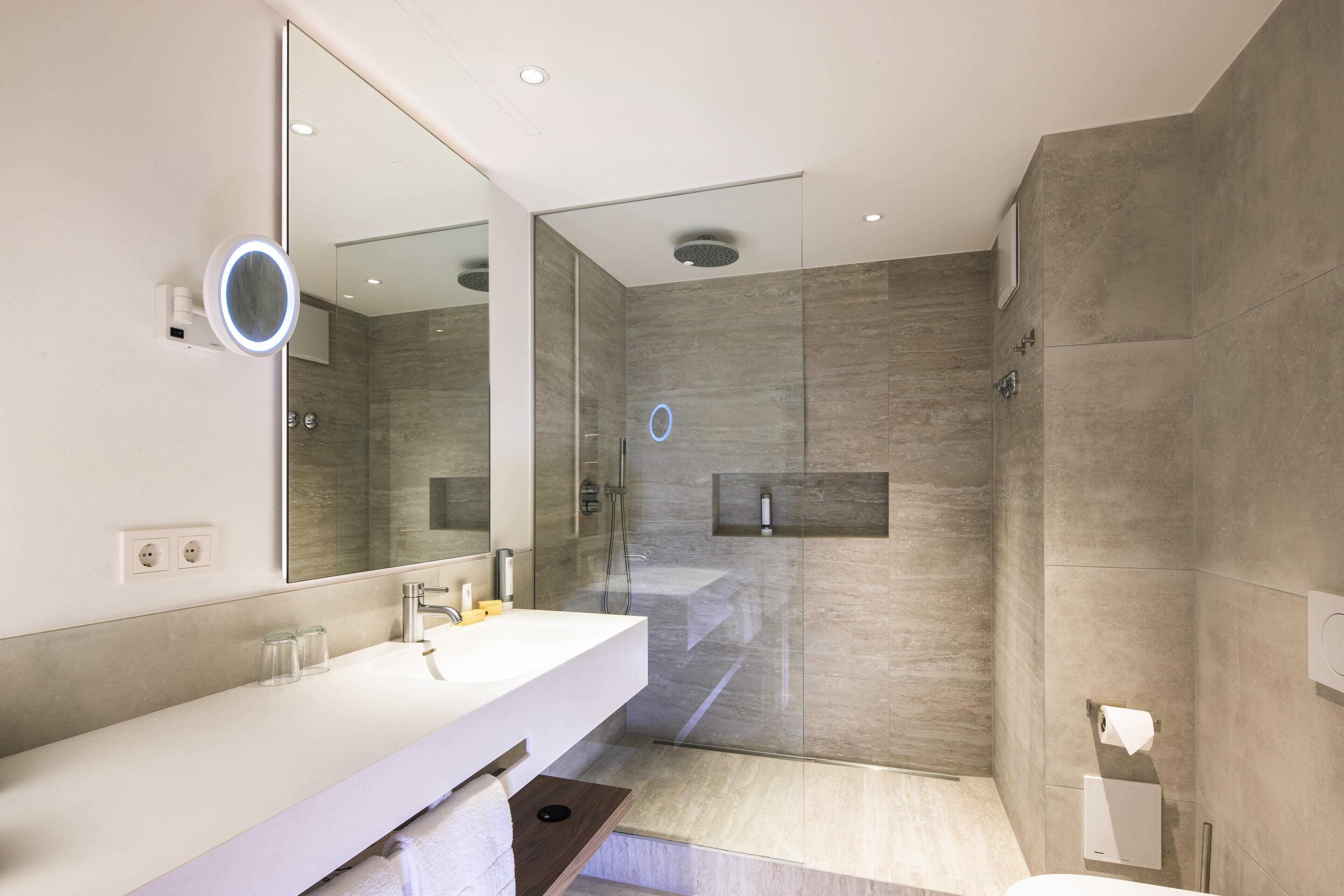 Un baño moderno con un espejo grande, un lavamanos blanco, una cabina de ducha con mampara de vidrio y un inodoro.