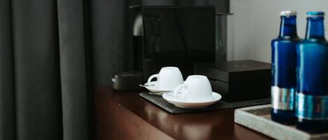 Una mesa de madera oscura con una cafetera, dos tazas blancas y dos botellas azules.