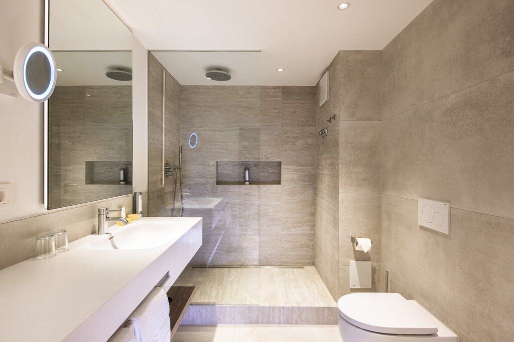 A modern bathroom with a large mirror, two sinks, a shower, and a toilet.