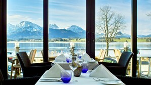 A dining table set with white tablecloths, blue glassware, and a decorative centerpiece. - Hotel Am Hopfensee (Fuessen)
