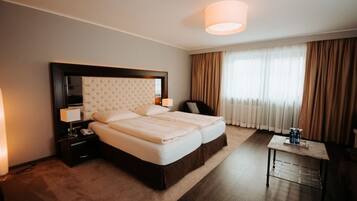 Habitación de hotel con una cama grande, una mesita de noche, una lámpara, una pequeña mesa con botellas y una ventana con cortinas.