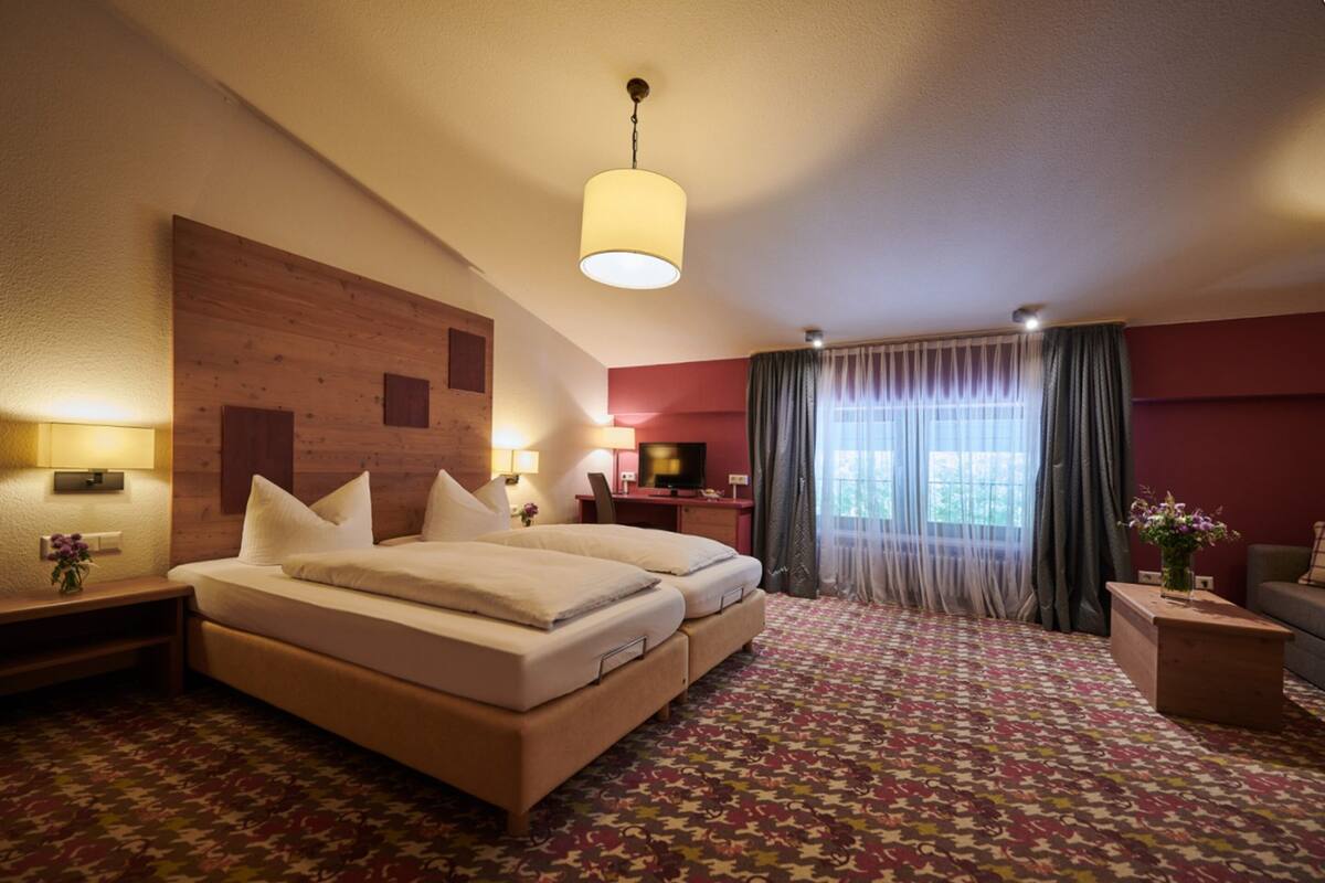 A hotel room with a large bed, a desk, a TV, and a window with curtains.