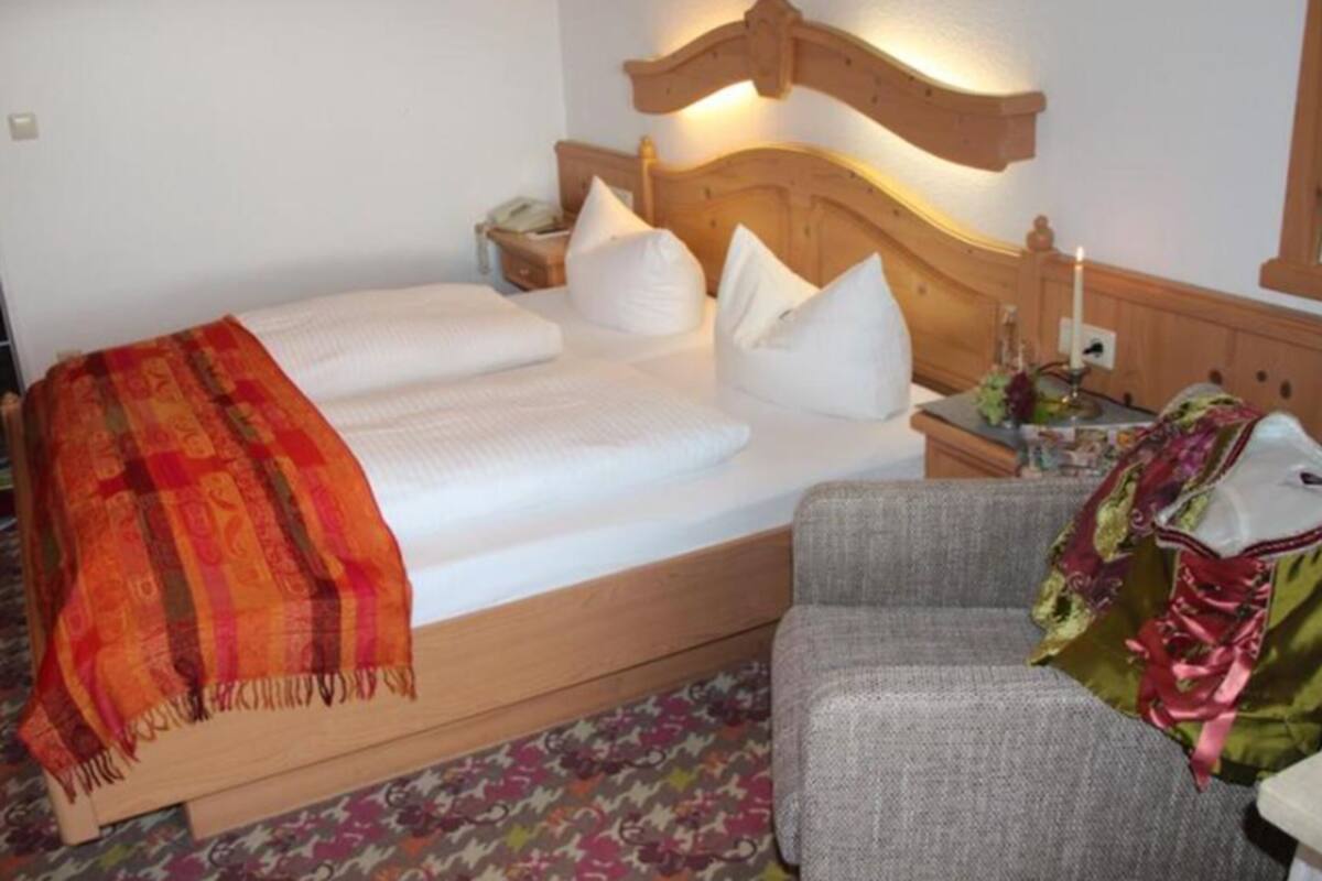A hotel room with a bed, a nightstand, a chair, and a bedside table with a lamp.