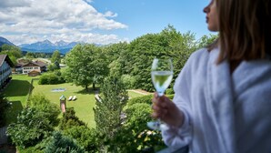 Una persona sosteniendo una copa de vino blanco, con vistas a un paisaje verde exuberante, cielo despejado y montañas a lo lejos.
