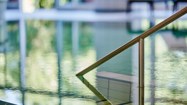 Vista despejada de una piscina con barrera de vidrio y barandilla metálica.