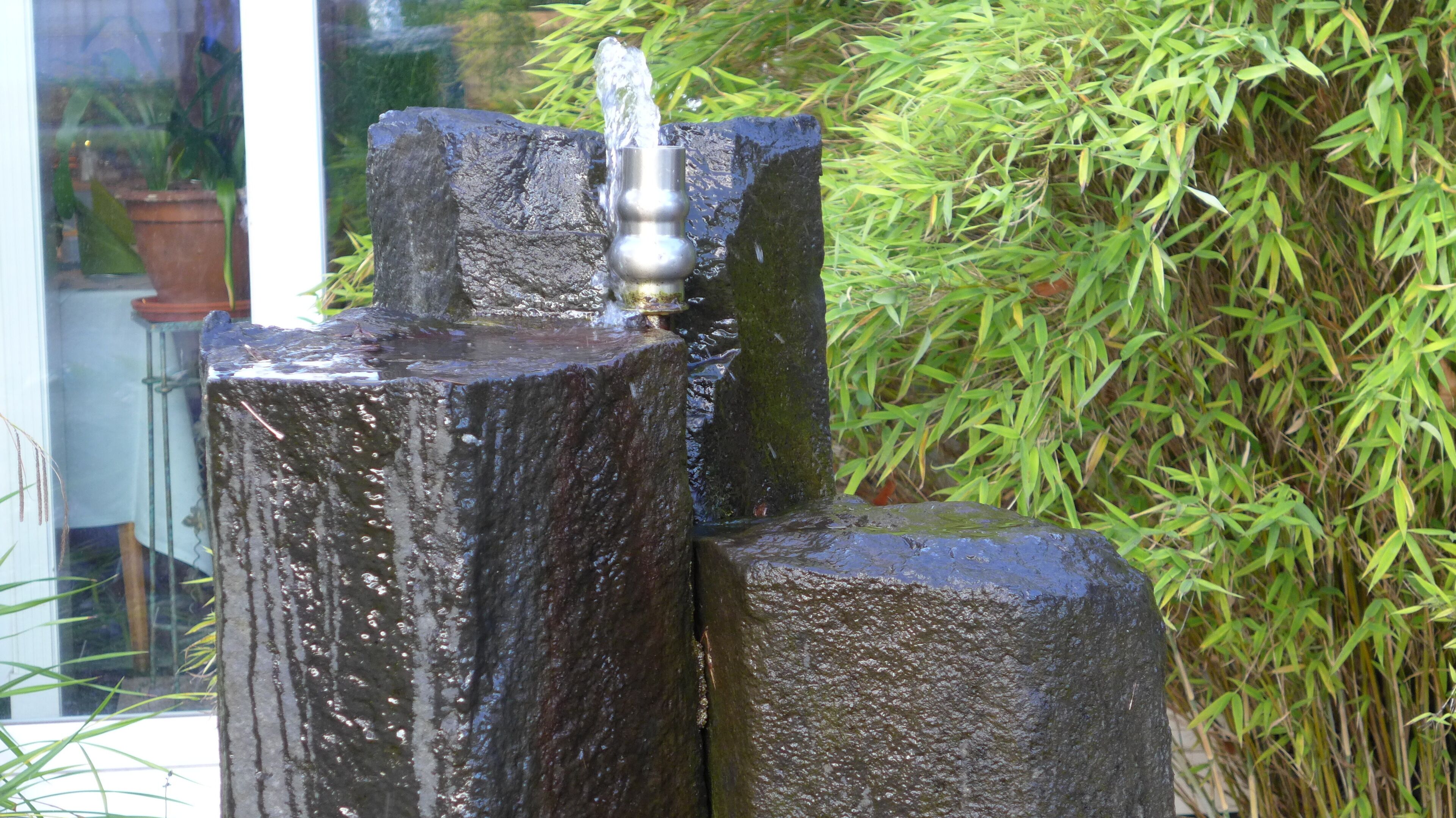 Ein Steinbrunnen mit Wasserspeier, umgeben von Bambuspflanzen.