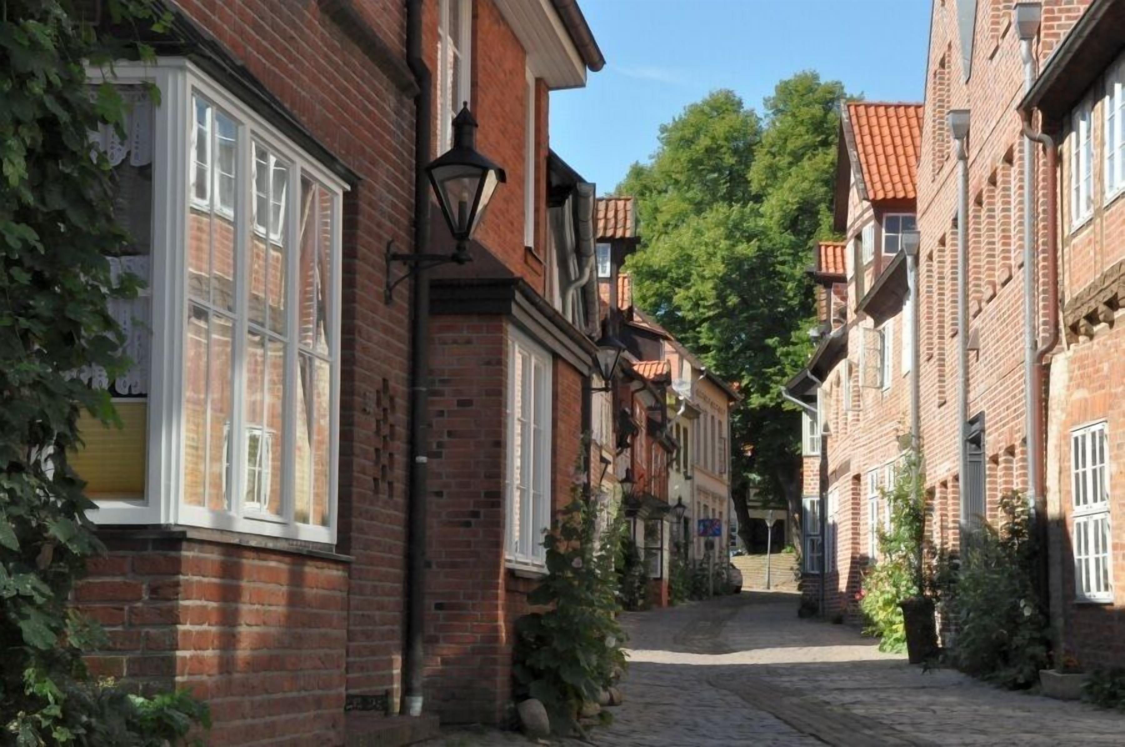 A narrow cobblestone street lined with traditional brick buildings, featuring large windows and hanging lanterns.
