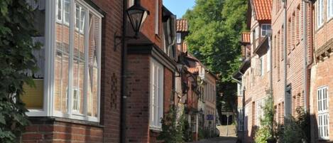 A narrow cobblestone street lined with traditional brick buildings, featuring large windows and hanging lanterns.
