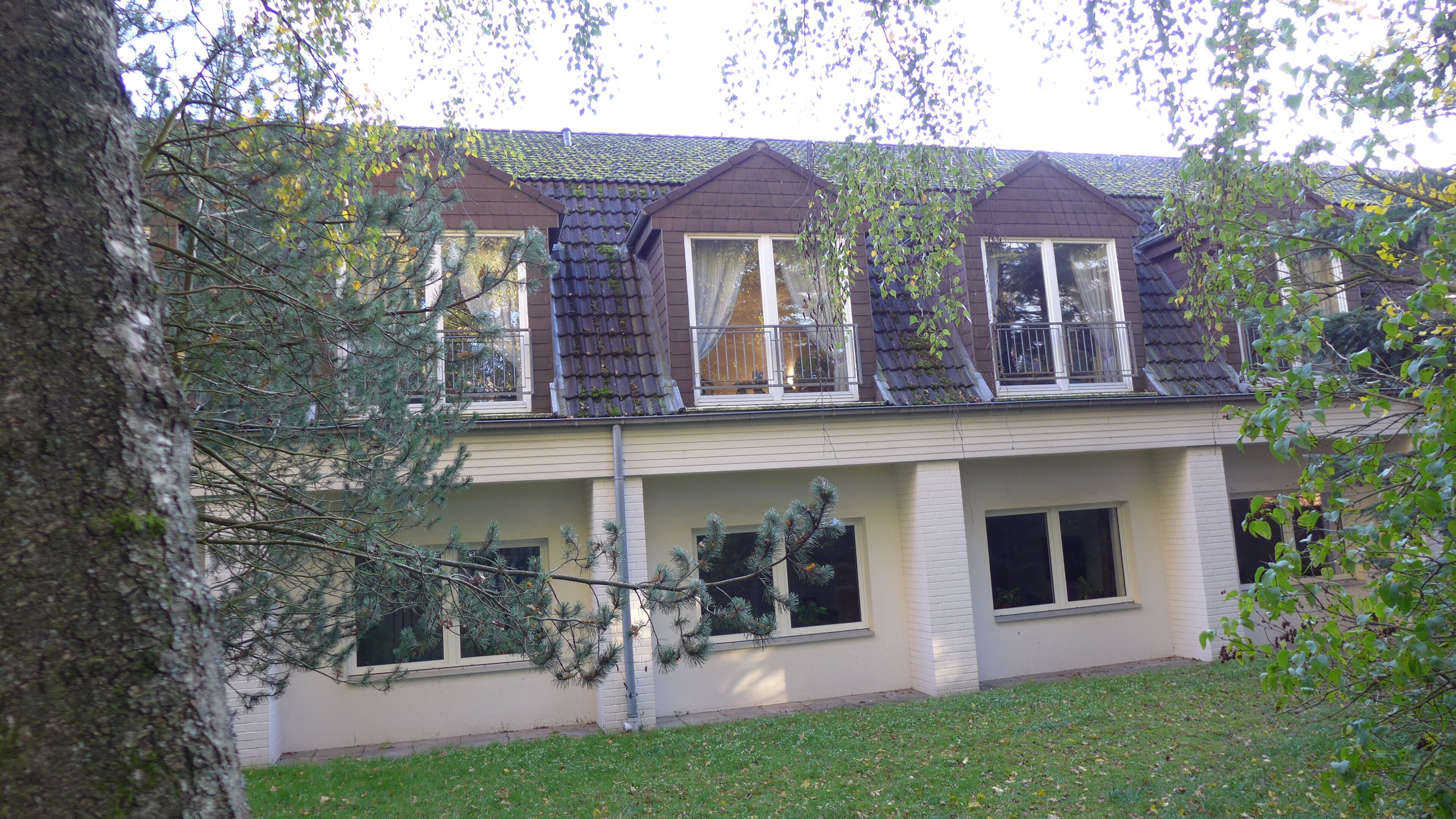 A two-story building with a dormer window, a balcony, and a tree in the foreground.