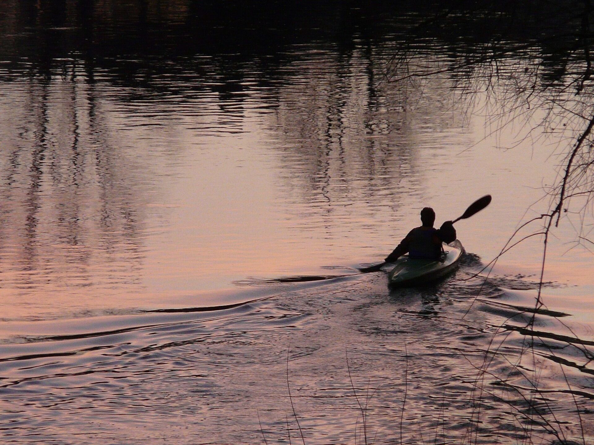 A person kayaking on a calm body of water during sunset.