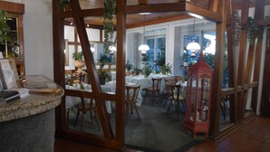 A restaurant with wooden beams, tables set for dining, and potted plants. - Hotel Heidpark (Lueneburg)