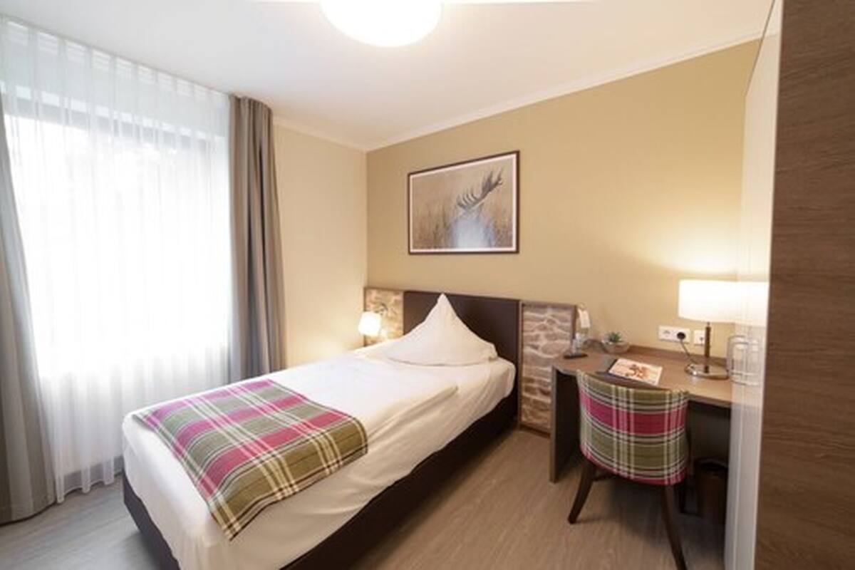 Une chambre d’hôtel avec un lit, un bureau, une chaise, une lampe et un tableau encadré au mur.