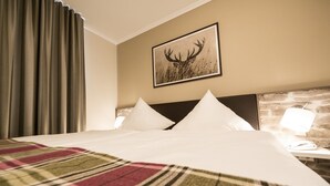 A hotel room with a large bed, a plaid blanket, a stone headboard, a wall-mounted picture of an elk, and a nightstand with a lamp.