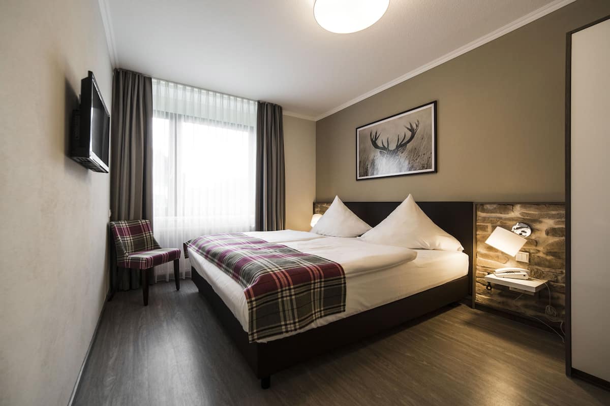 Une chambre d’hôtel avec un lit, une chaise, un téléviseur à écran plat, une lampe et un tableau au mur.
