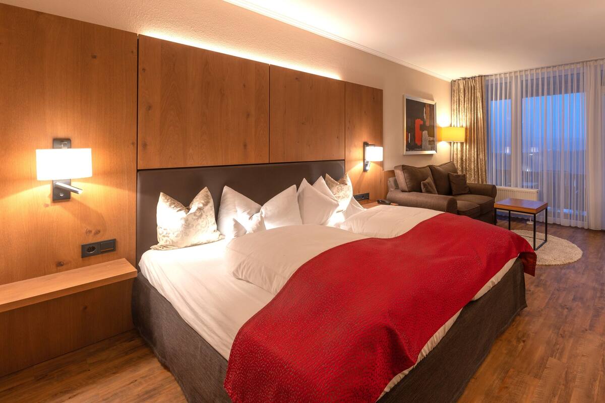 A hotel room with a large bed, a desk, a chair, and a sofa.