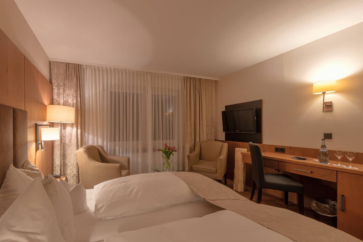 A hotel room with a bed, two armchairs, a desk, a TV, and a lamp.