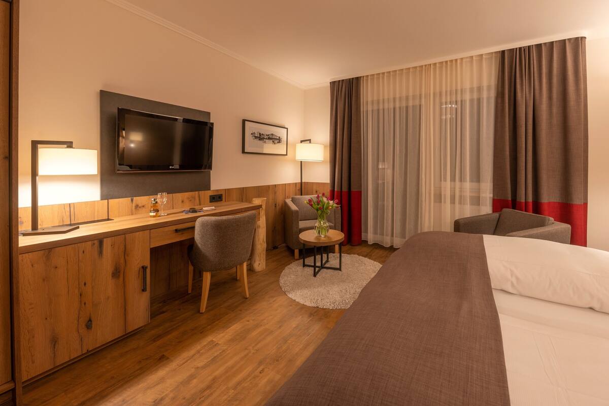 A hotel room with a wooden desk, a television, a bed, and a chair.