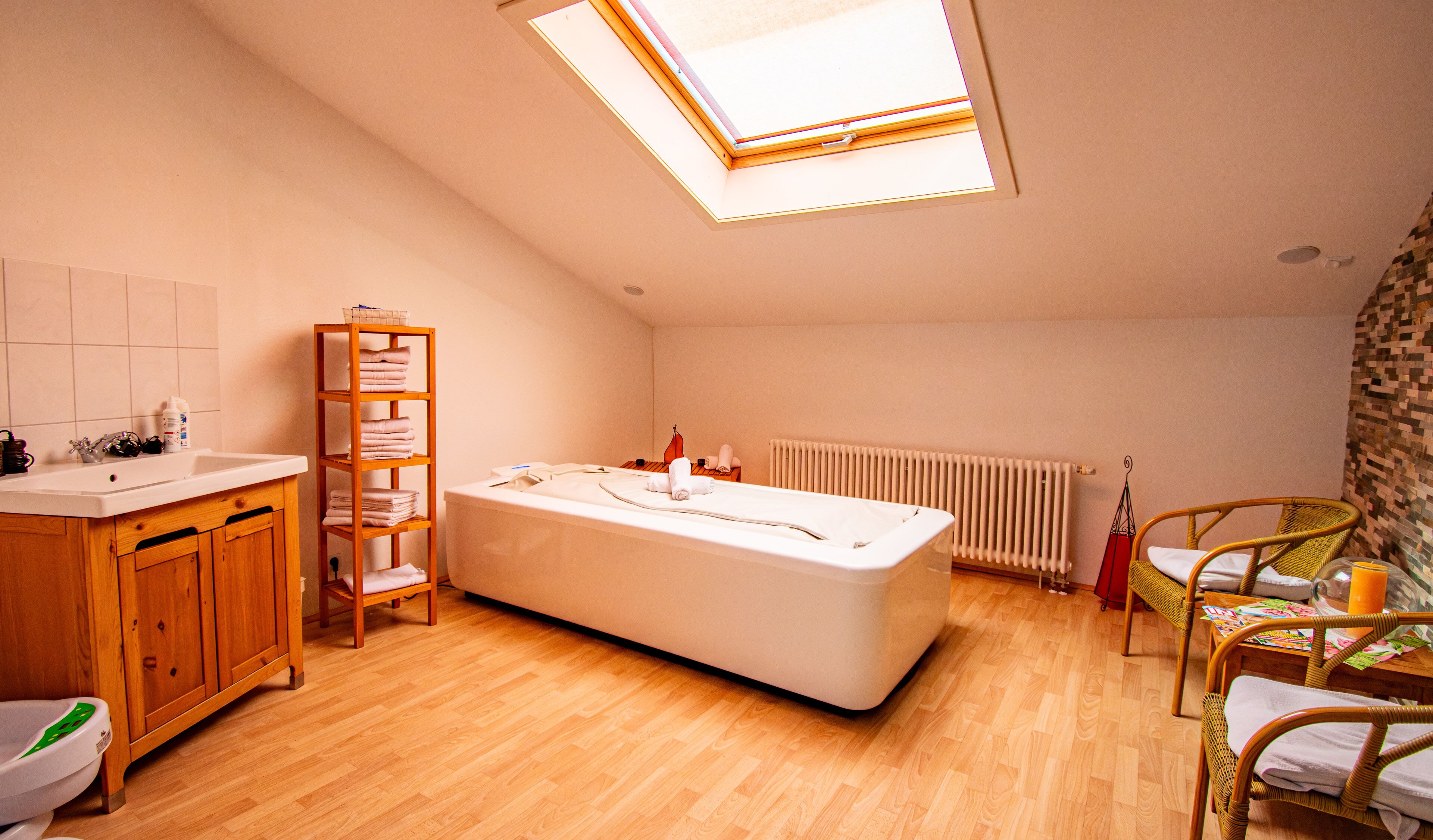 Un baño con tragaluz, bañera, armarios de madera y una silla de mimbre.