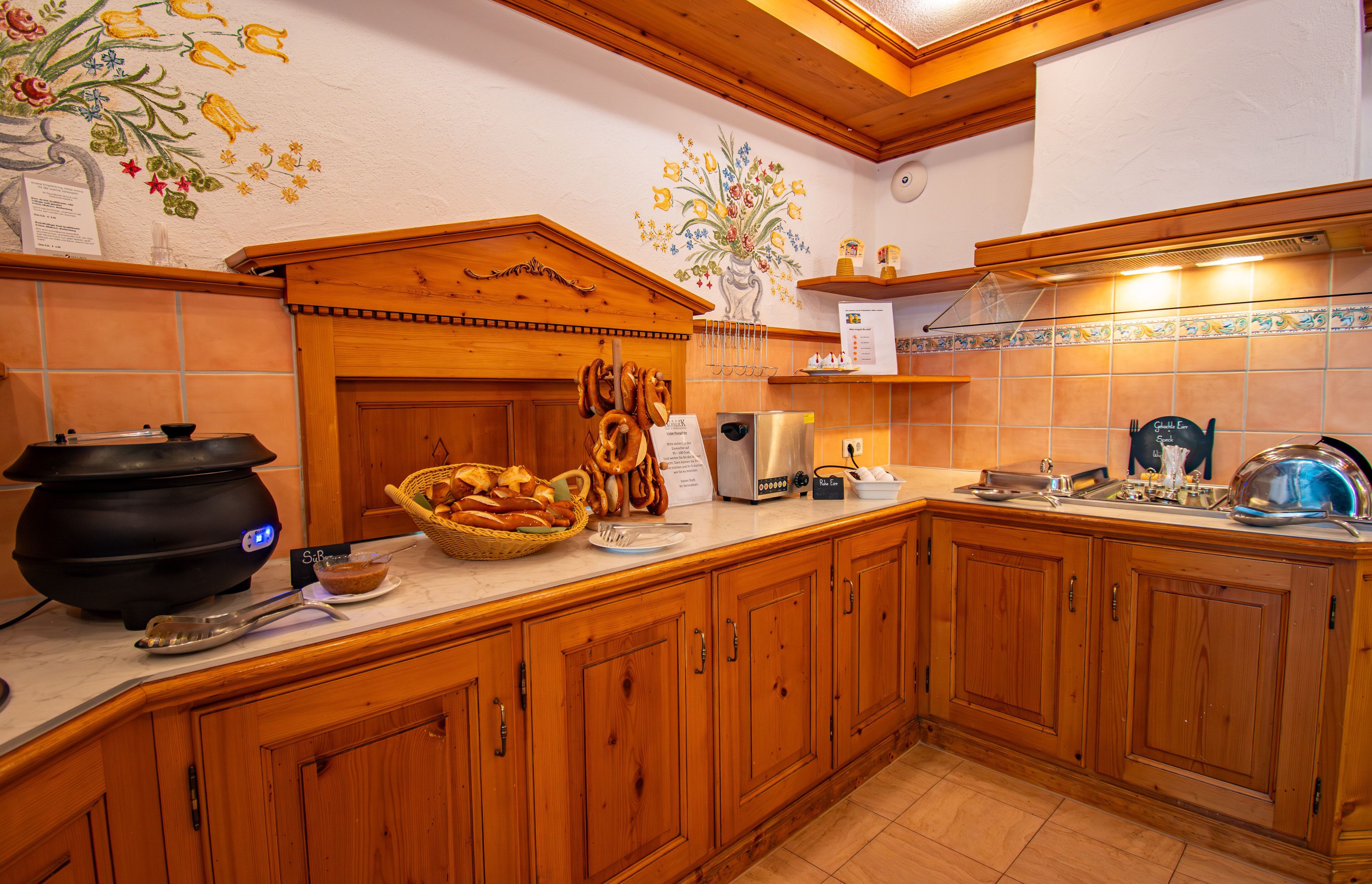 A kitchen with wooden cabinets, a black cooking pot, a basket of bread, and a decorative wall mural.