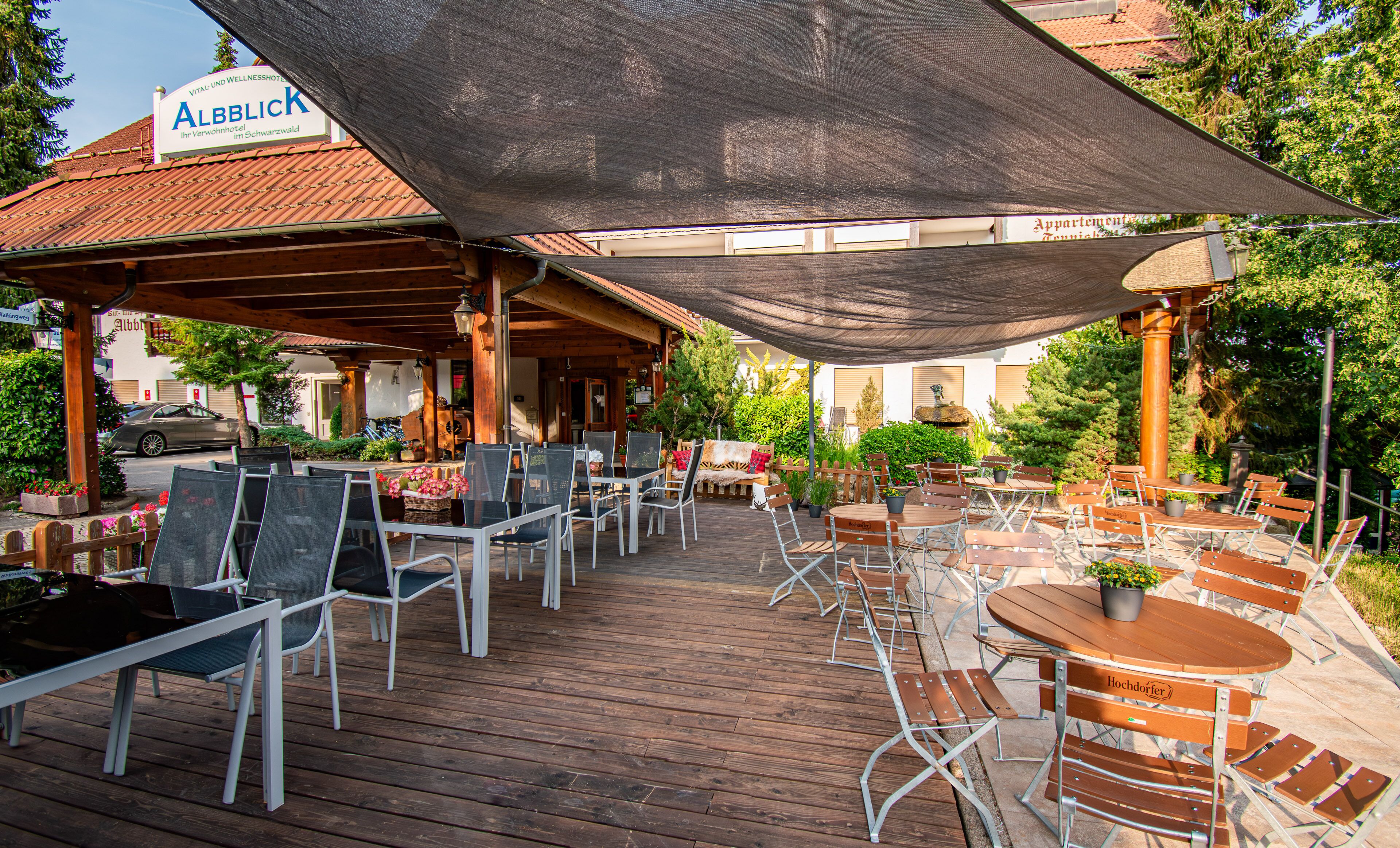 An outdoor patio with wooden tables and chairs, a covered seating area, and a sign for 'Albblick'.