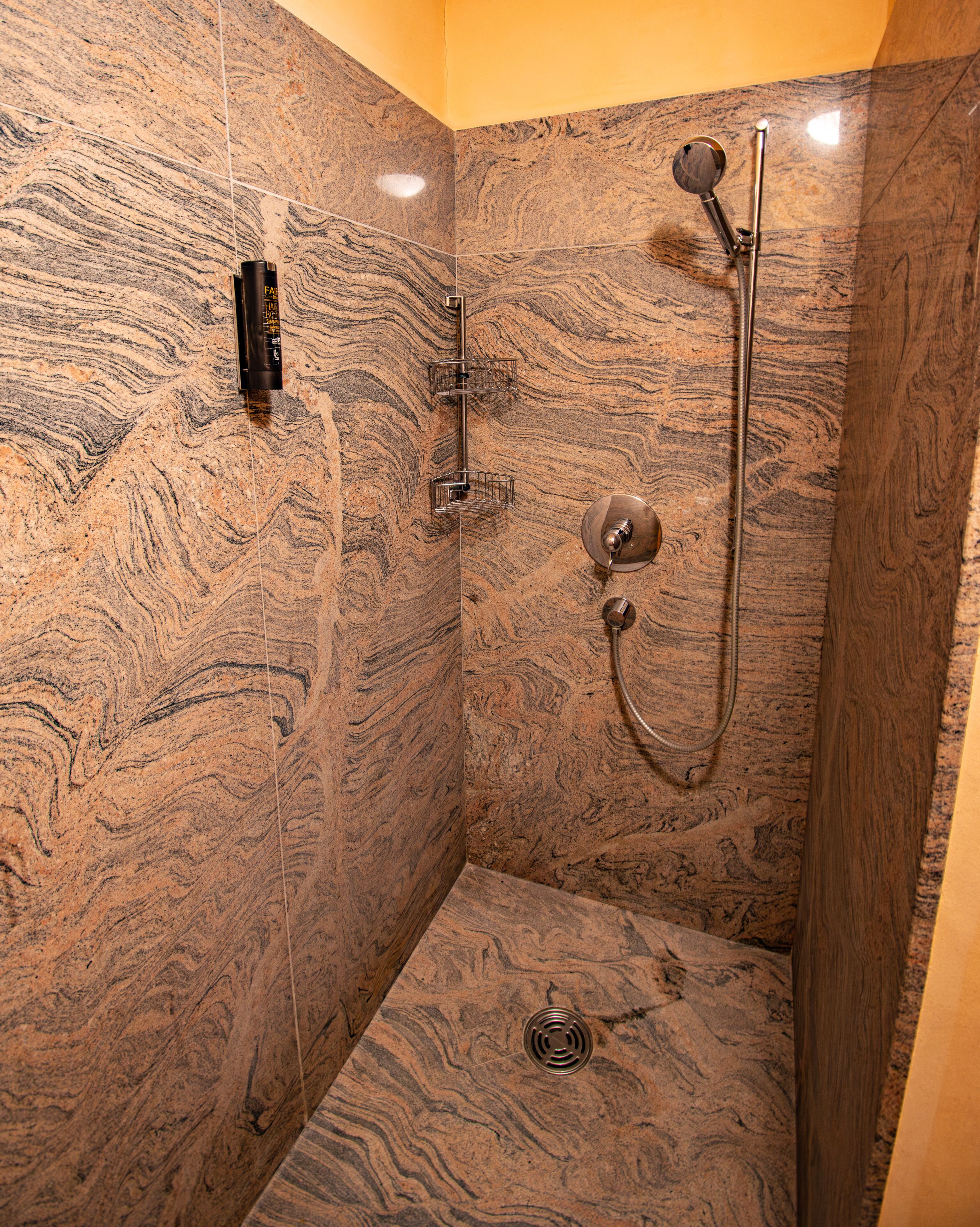 A shower with a marble wall, a handheld showerhead, and a wall-mounted faucet.