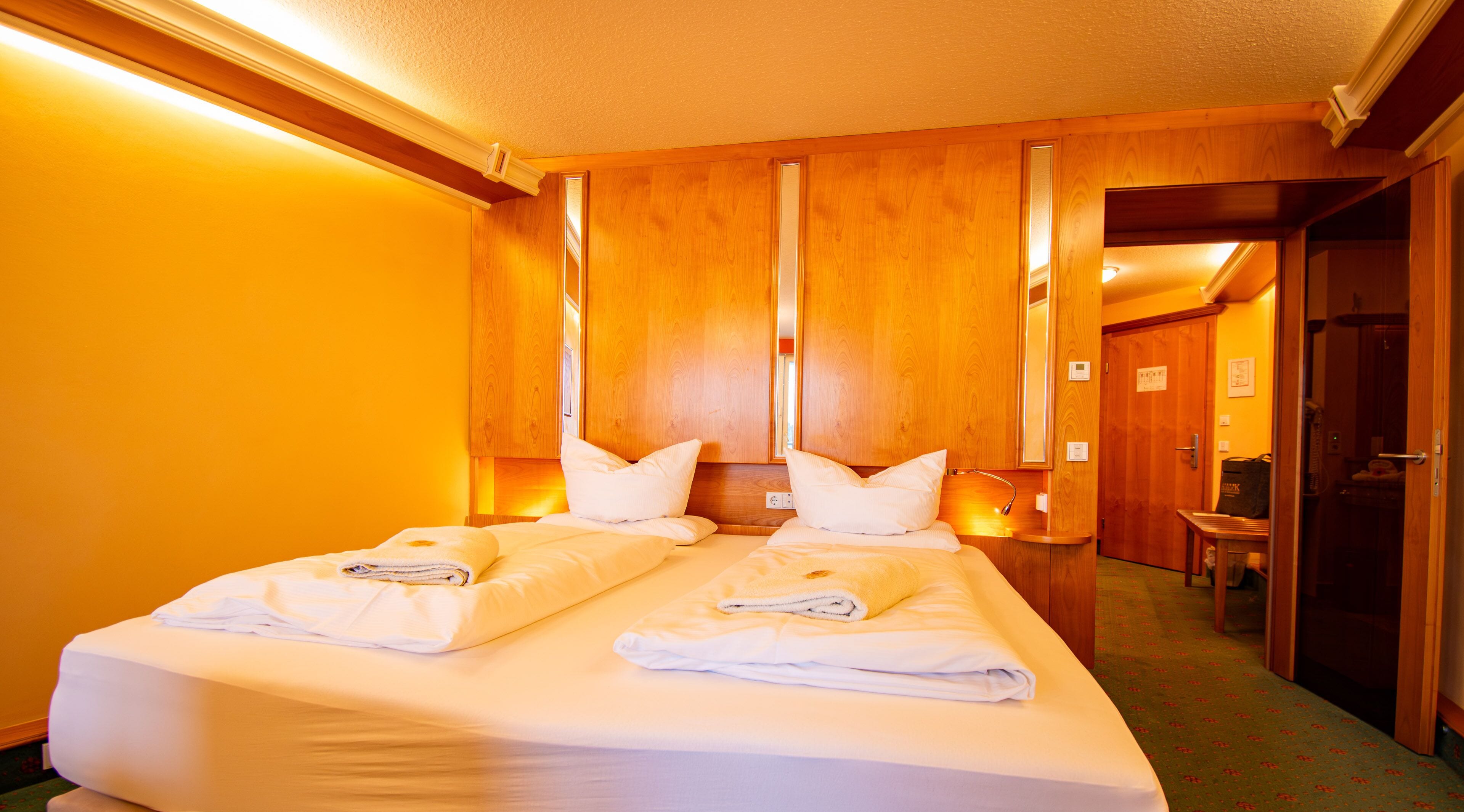 Una habitación de hotel con una cama grande, paneles de madera, un espejo y un banco.