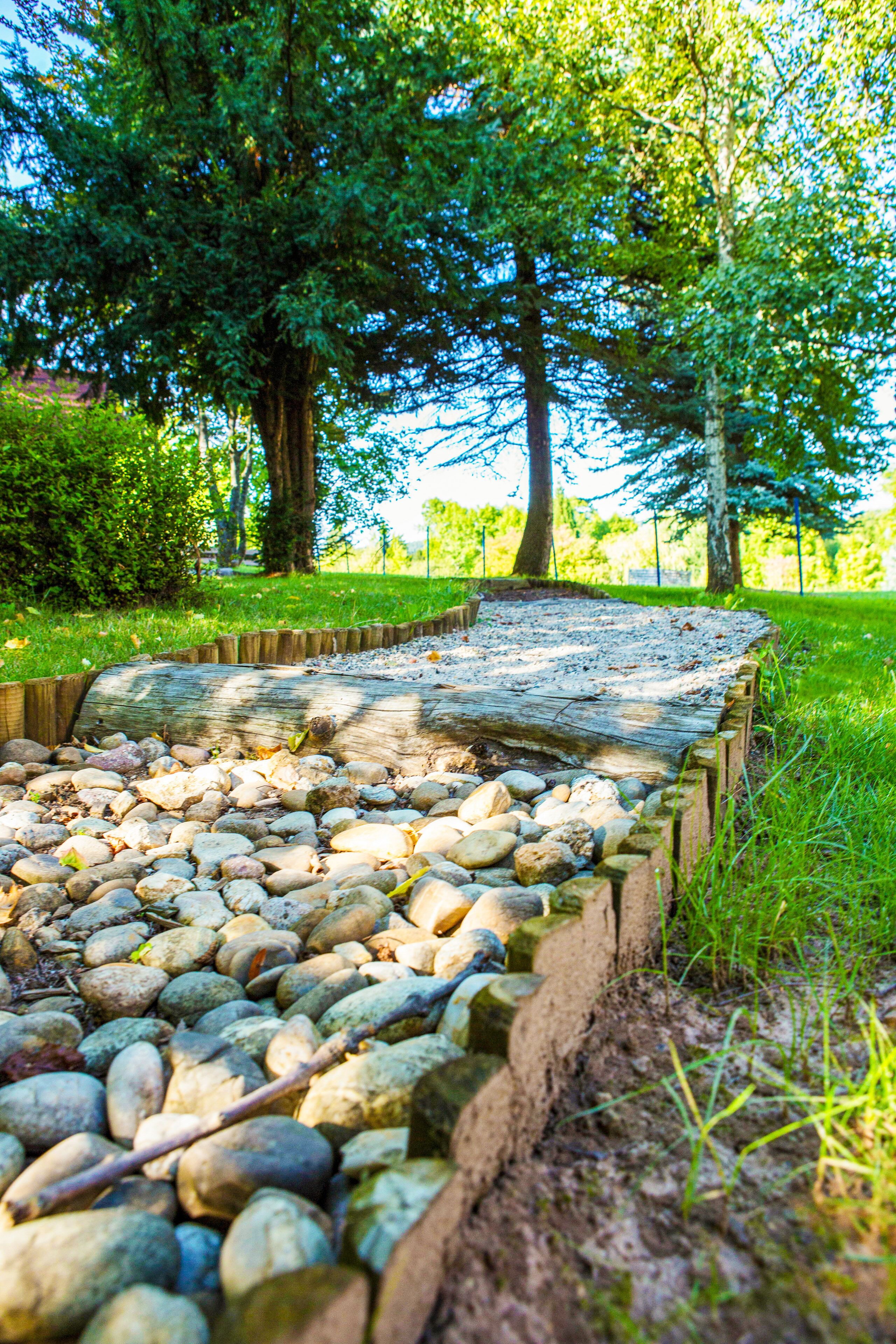 A stone pathway with a wooden border, surrounded by grass and trees.