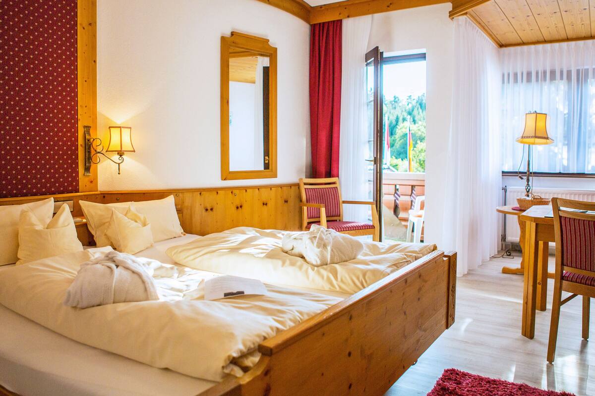 Une chambre à coucher avec un lit en bois, une chaise, une table et une fenêtre avec des rideaux.