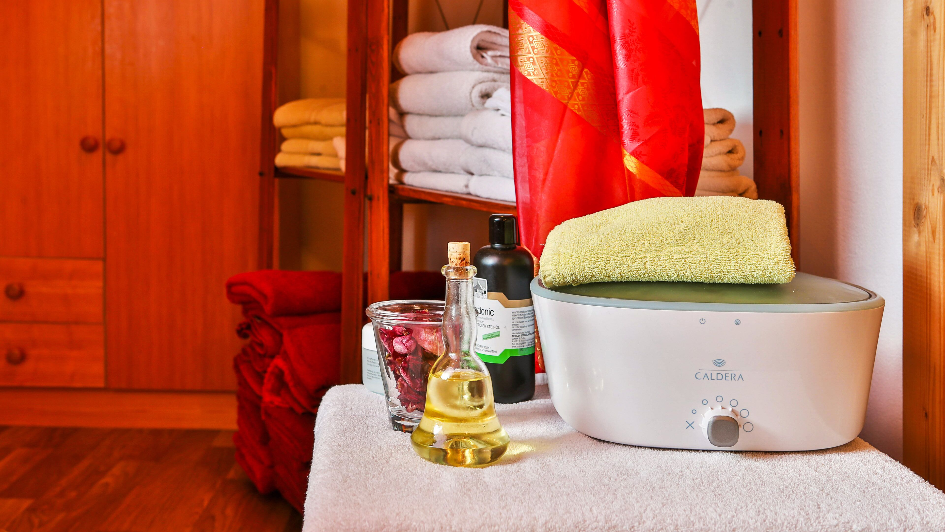 A bathroom with a white bathtub, a bottle of oil, a bottle of lotion, and a towel on a shelf.