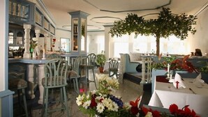 A restaurant with a rustic interior, featuring wooden chairs, tables set for dining, and a large indoor tree. - Kur- und Wellness Hotel Mönchgut (Göhren)