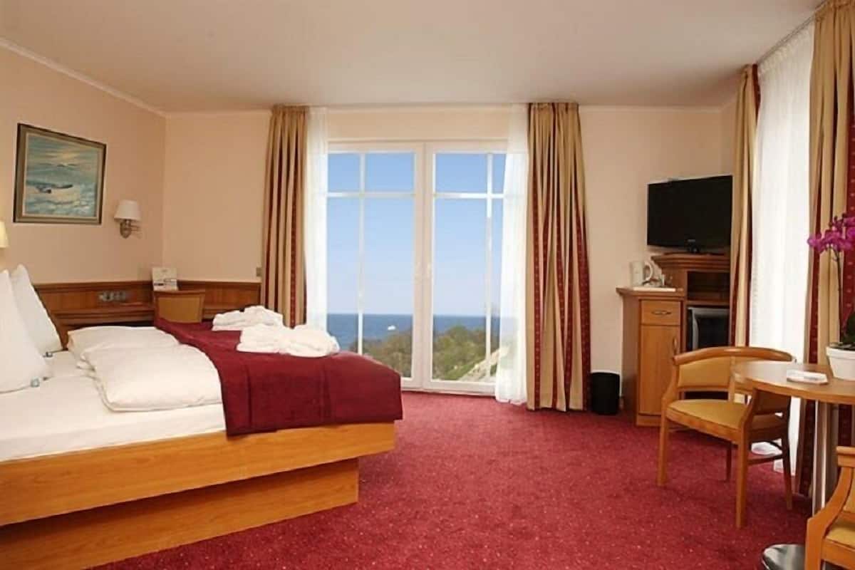 A hotel room with a bed, a desk, a television, and a view of the outdoors.