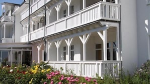 A white multi-story building with balconies and a garden with colorful flowers. - Kur- und Wellness Hotel Mönchgut (Göhren)