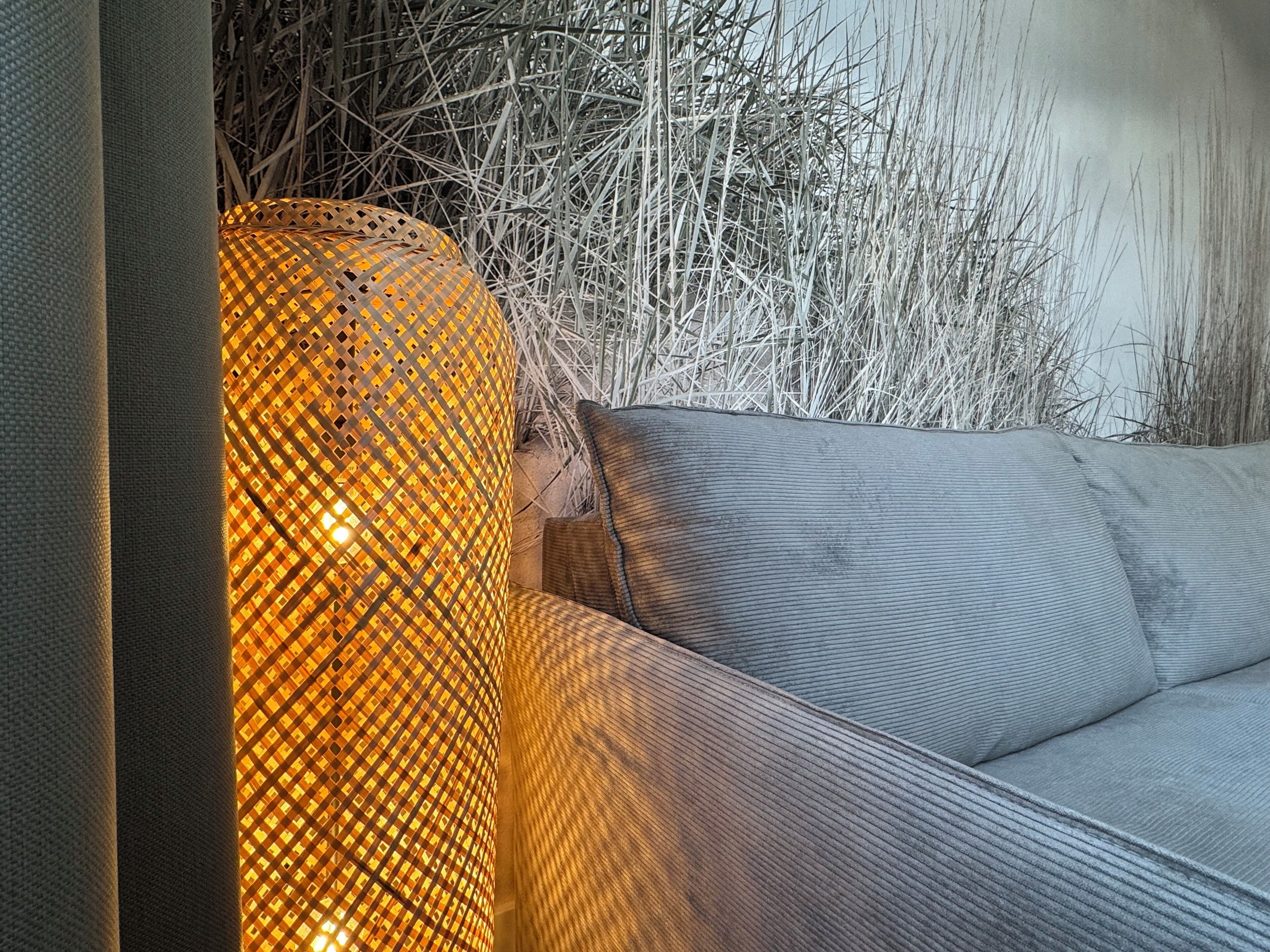 A grey sofa with a textured fabric and a woven, illuminated lamp beside it.