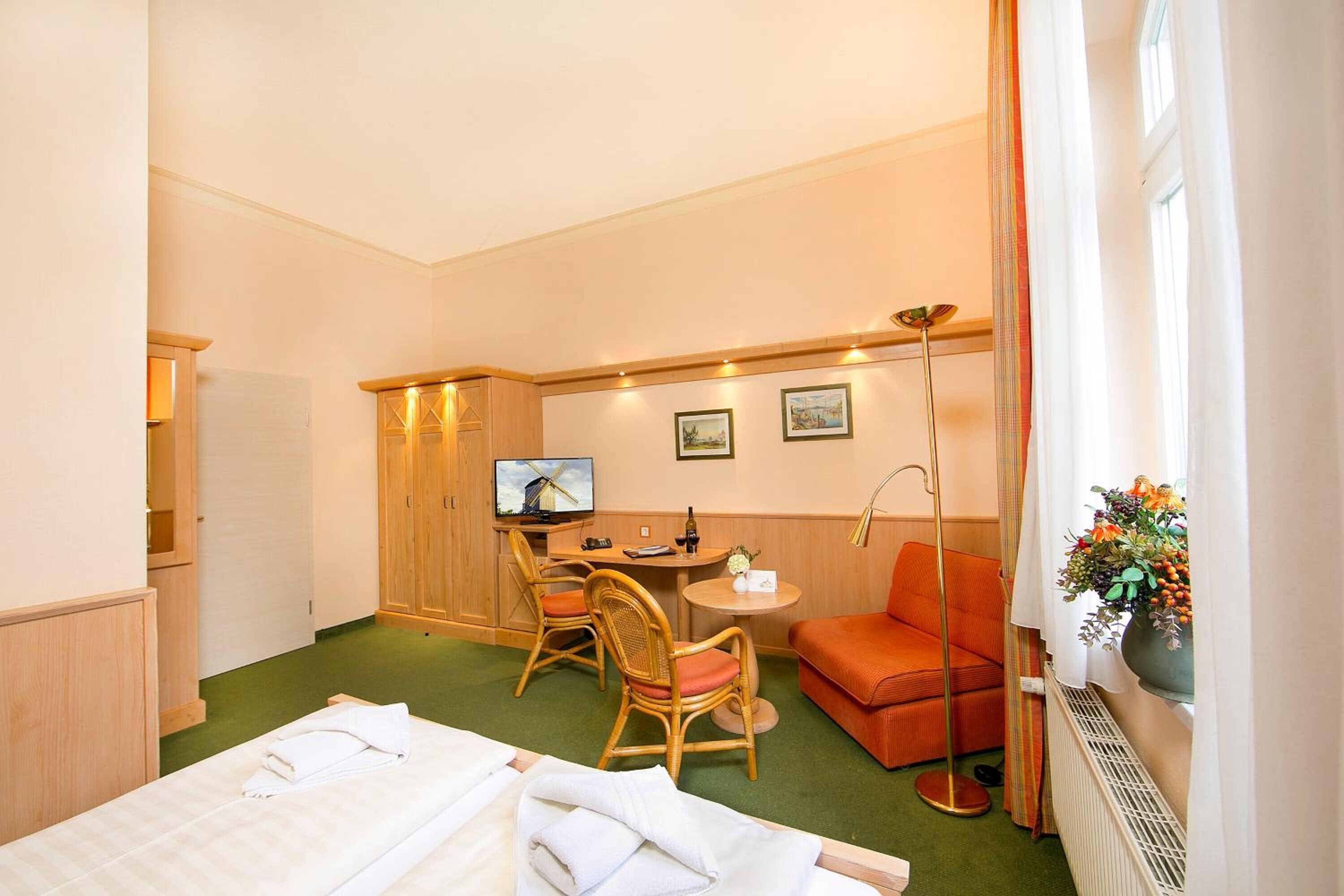 Habitación de hotel con cama, escritorio con silla, una mesita, sofá y ventana con cortinas.