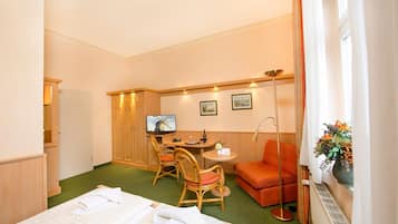 Habitación de hotel con cama, escritorio con silla, una mesita, sofá y ventana con cortinas.