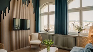 A modern living room with a TV mounted on a wooden panel wall, a sofa, a chair, and a coffee table. - Dünenschloß (Zinnowitz)