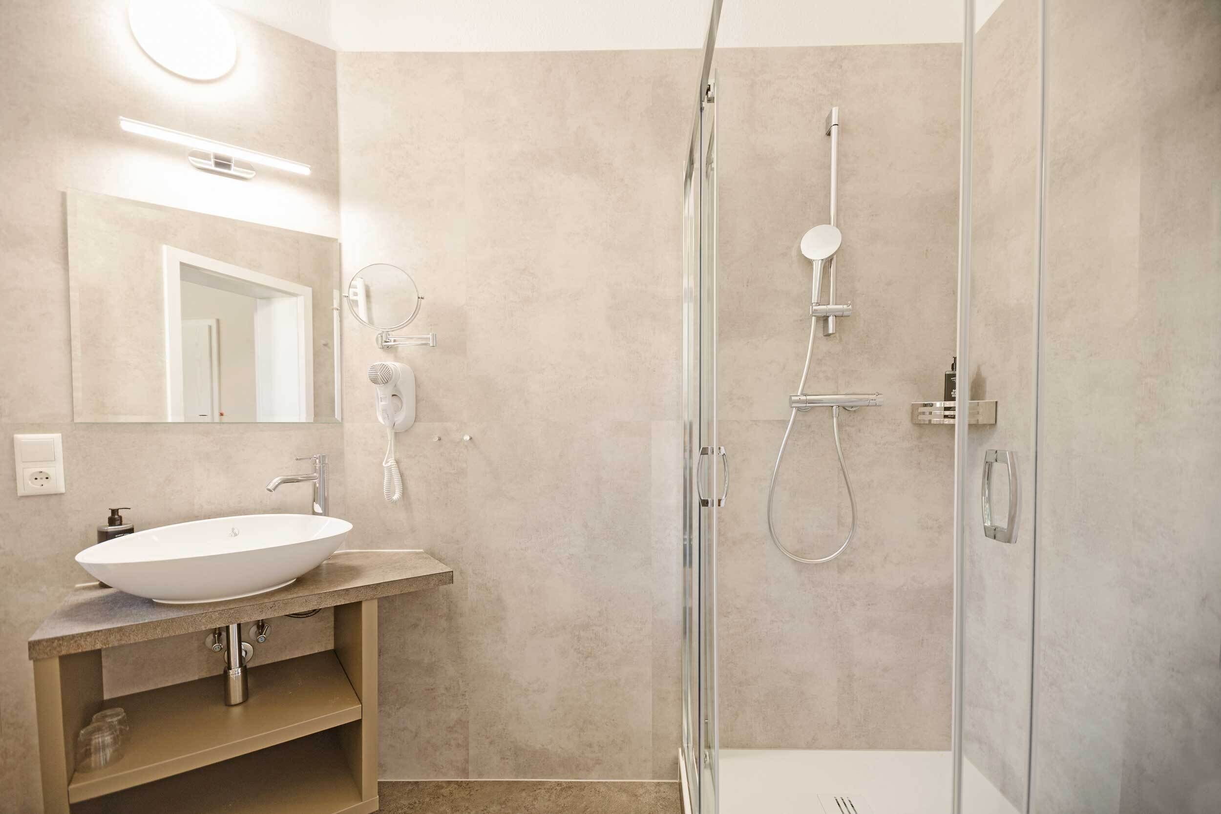 A modern bathroom with a large oval sink, a glass-enclosed shower, and a mirror with a round light.
