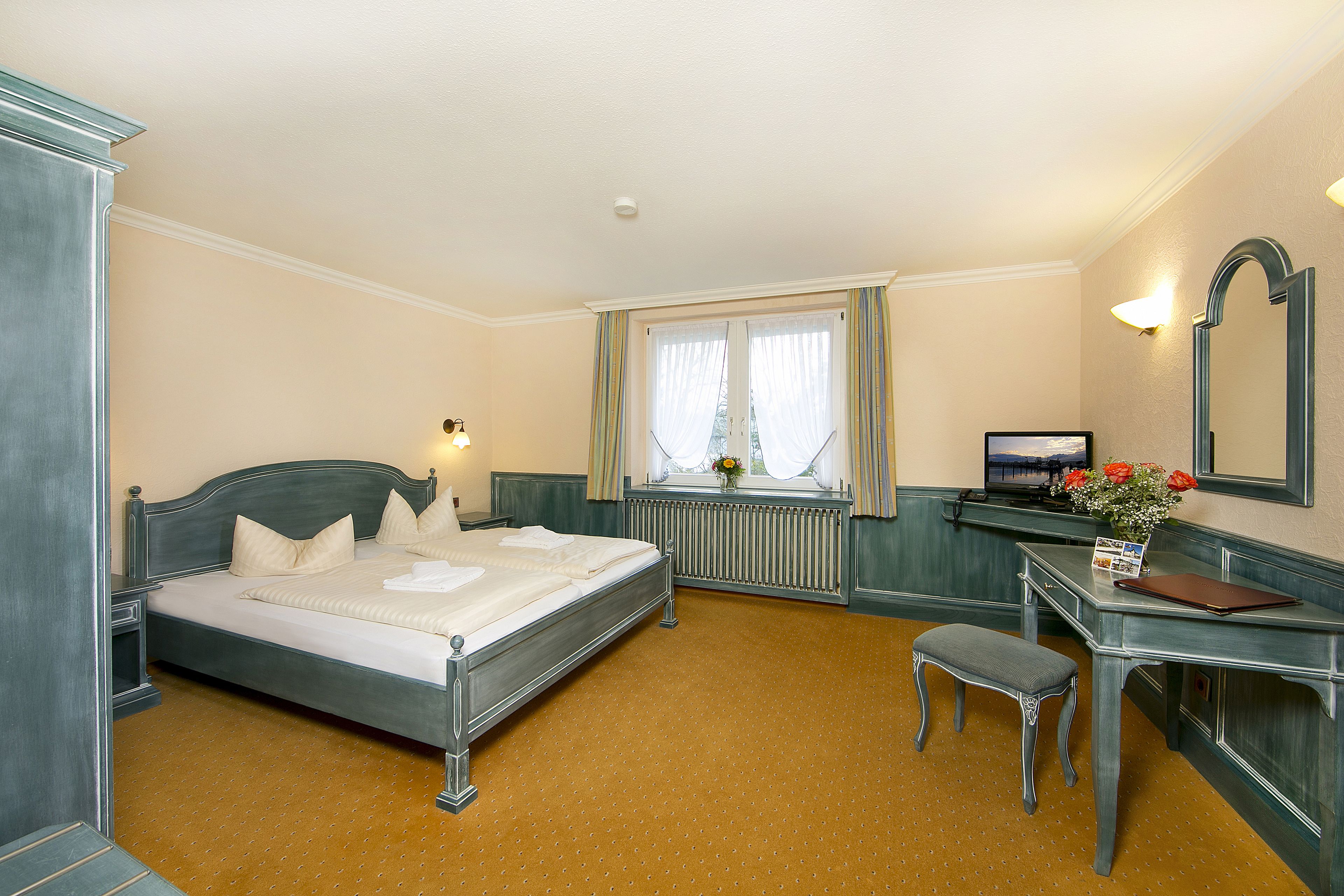 A bedroom with a bed, a desk, a chair, a window with curtains, and a radiator.