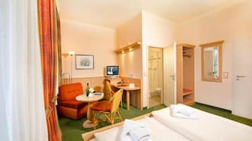 A hotel room with two beds, a desk, a chair, a small table, a shower area, and a wardrobe.