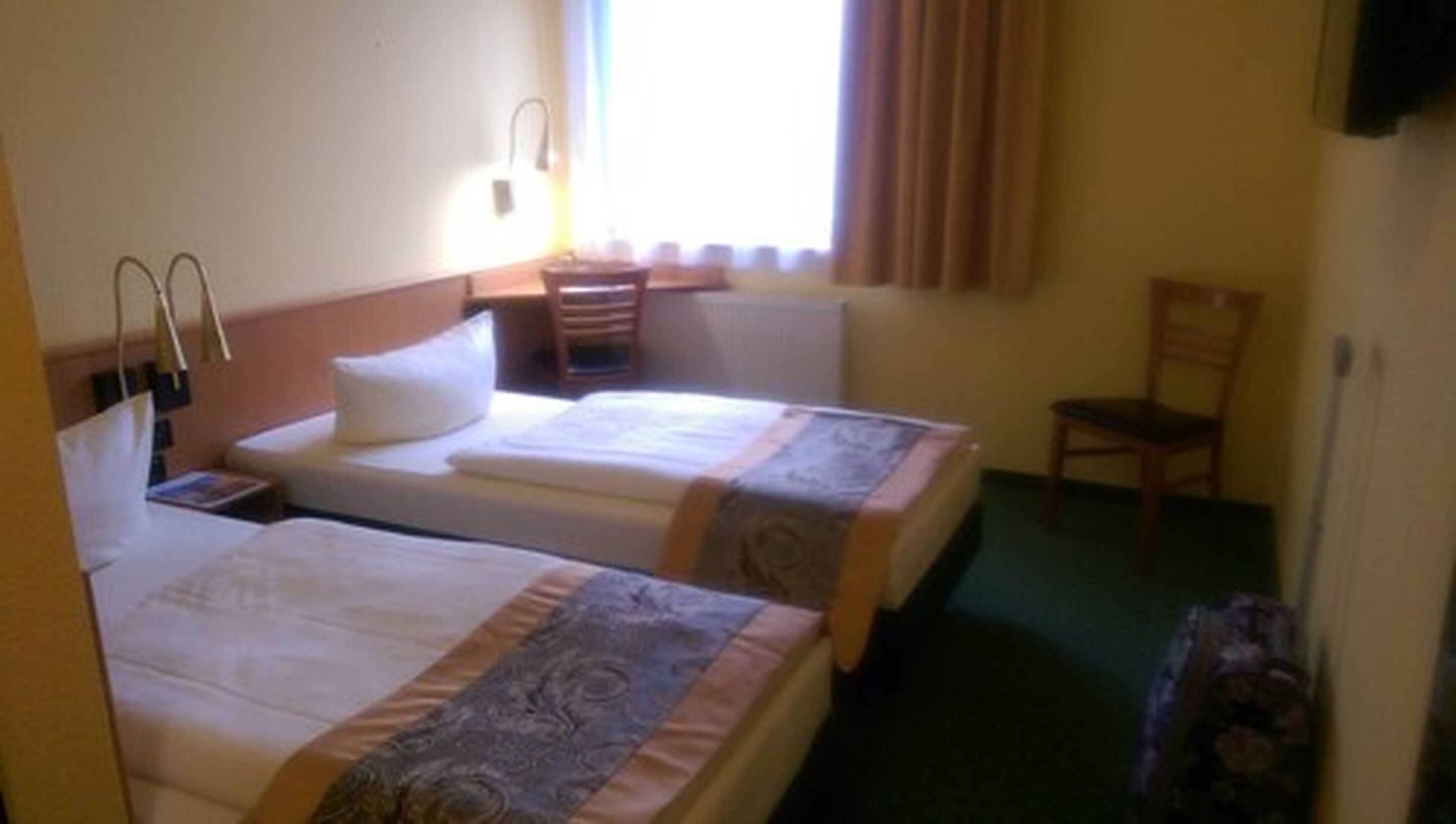 Ein Hotelzimmer mit zwei Einzelbetten, einem Nachttisch, einem Sessel und einem Fenster mit Vorhängen.