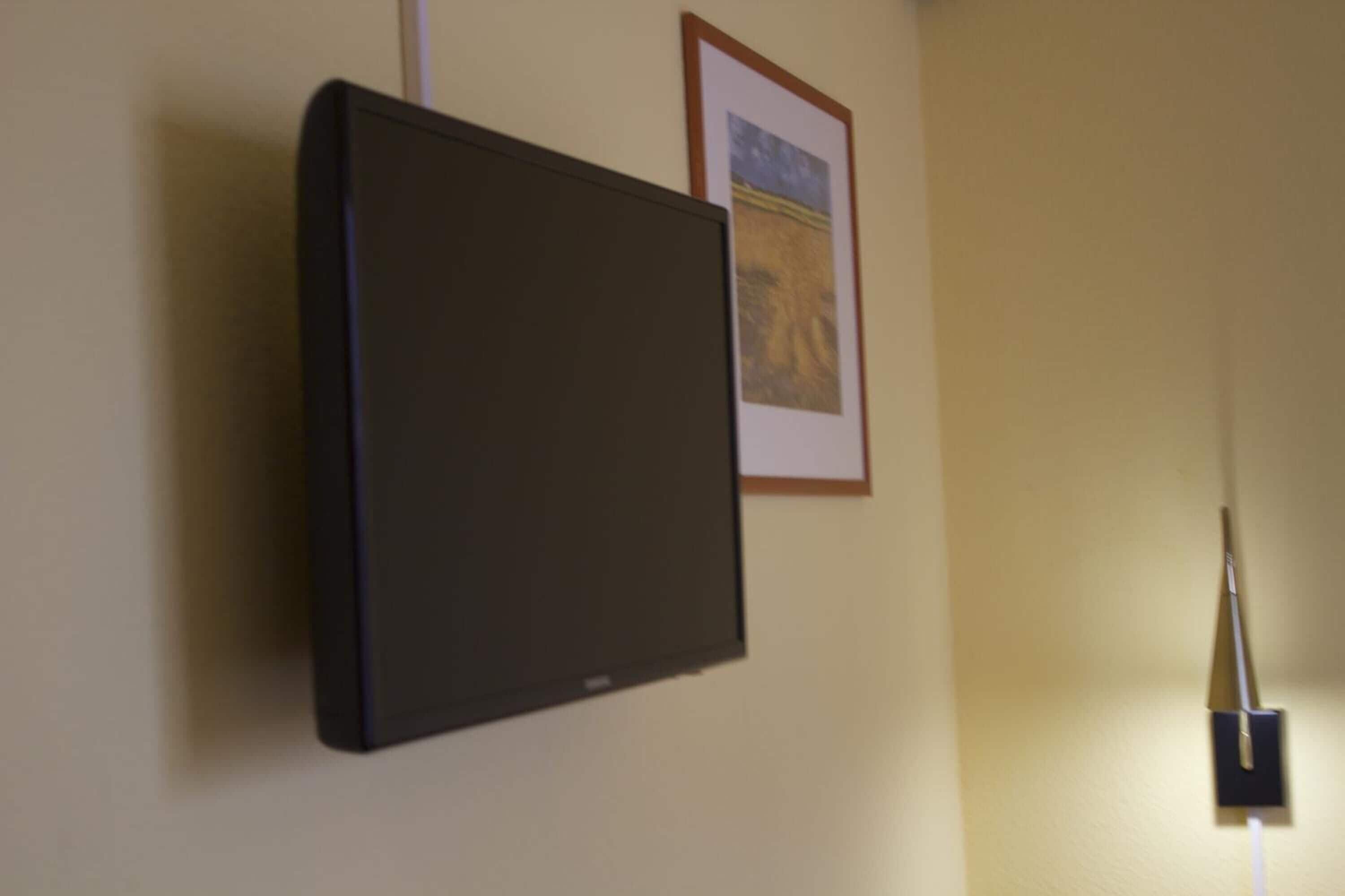 A flat-screen TV mounted on a wall with a framed picture above it.