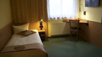 Ein Hotelzimmer mit einem Bett, einem Schreibtisch, einem Stuhl, einem Heizkörper und einem an der Wand befestigten Fernseher.