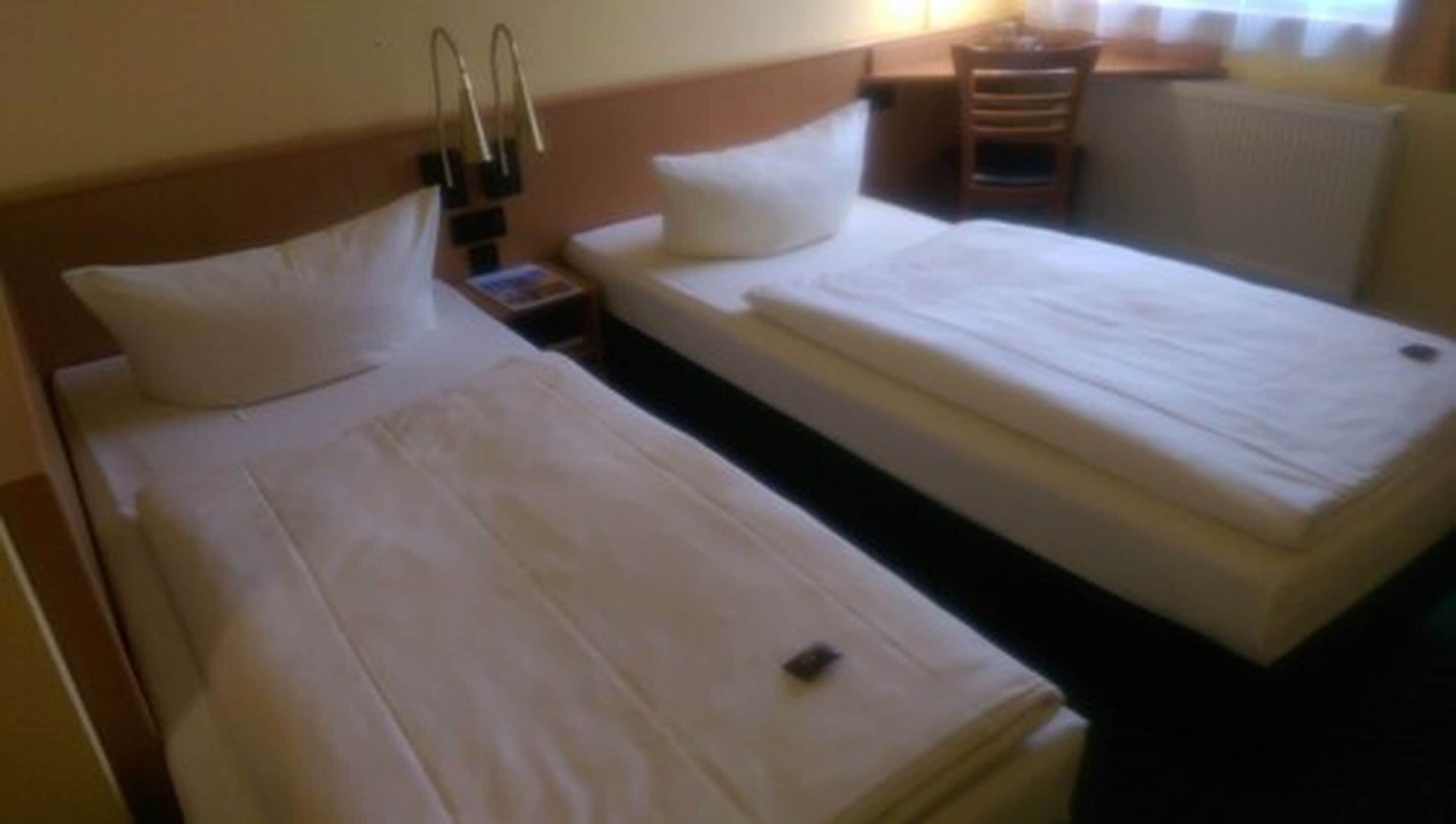A hotel room with two single beds, a nightstand, a lamp, and a chair.