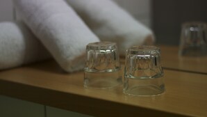 Un tavolo in legno con due bicchieri di vetro trasparenti e due asciugamani bianchi arrotolati.
