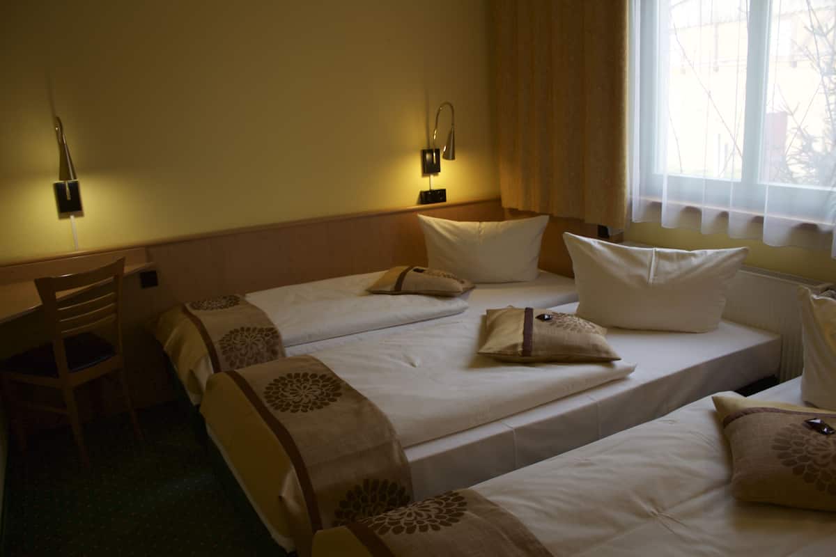 A hotel room with two beds, a chair, and two wall-mounted lamps.